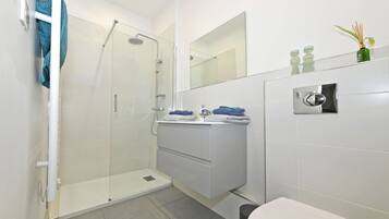 A modern bathroom with a glass shower enclosure, a white sink with a mirror above, and a toilet.