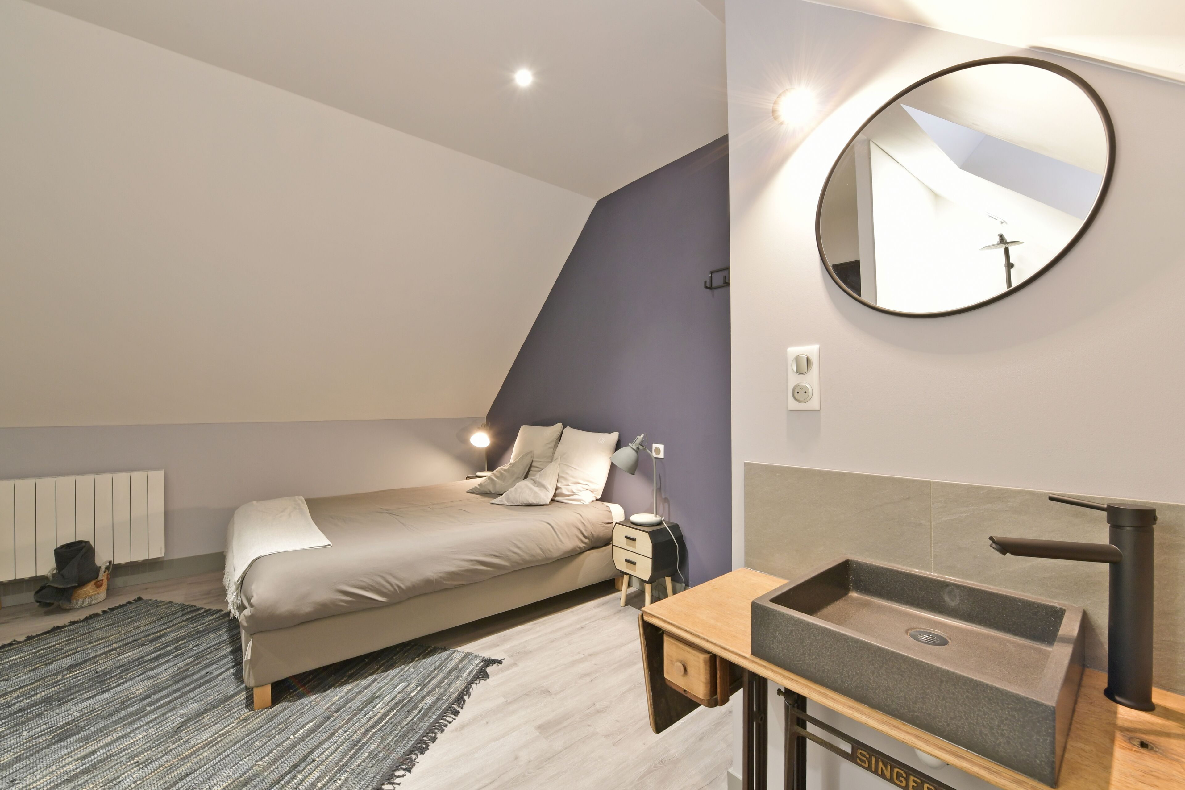 A modern bedroom with a bed, bedside table, and a round mirror.