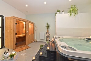 A spa area with a wooden sauna, a hot tub, and a small seating area with candles. - Les Nuits Pastel (Saint-Quentin)