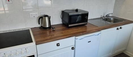 A compact kitchen with white cabinets, a microwave, a kettle, a sink, and a dishwasher.