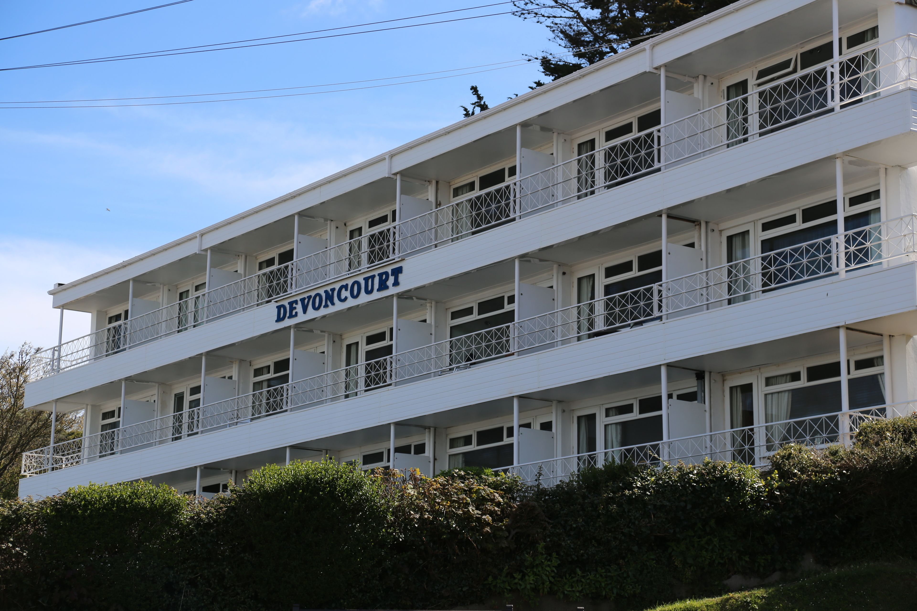 Un edificio de varios pisos con balcones y el nombre "DEVONCOURT" a la vista.