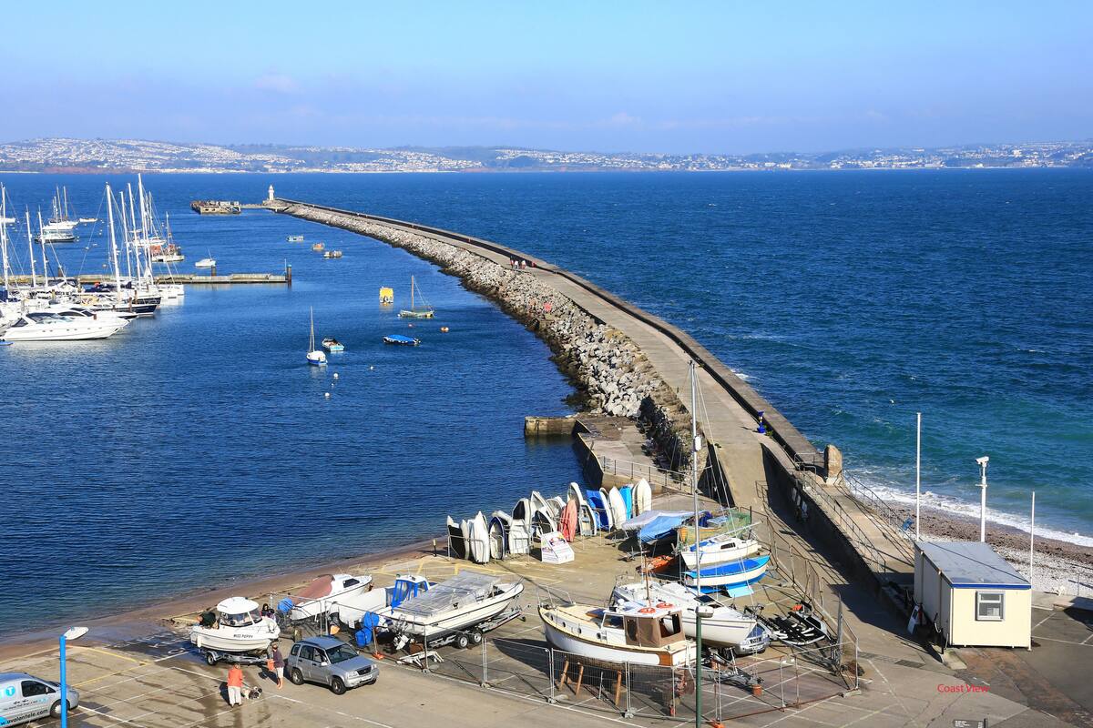 A coastal marina with boats docked, a pier extending into the water, and a small building near the shore.