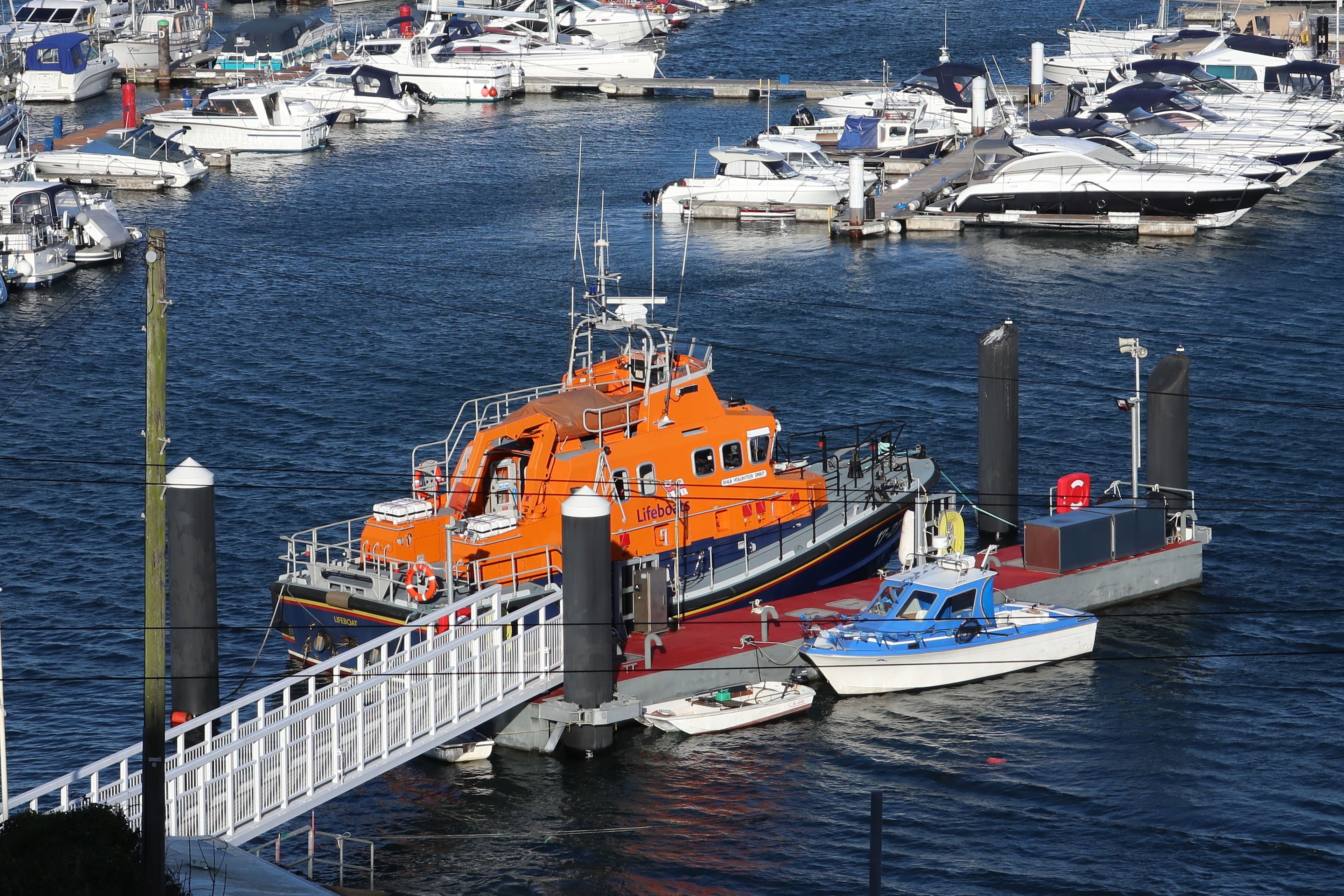 A marina with various boats docked, including a prominent orange lifeboat.