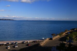 A coastal parking area with vehicles and a road leading to the beach.