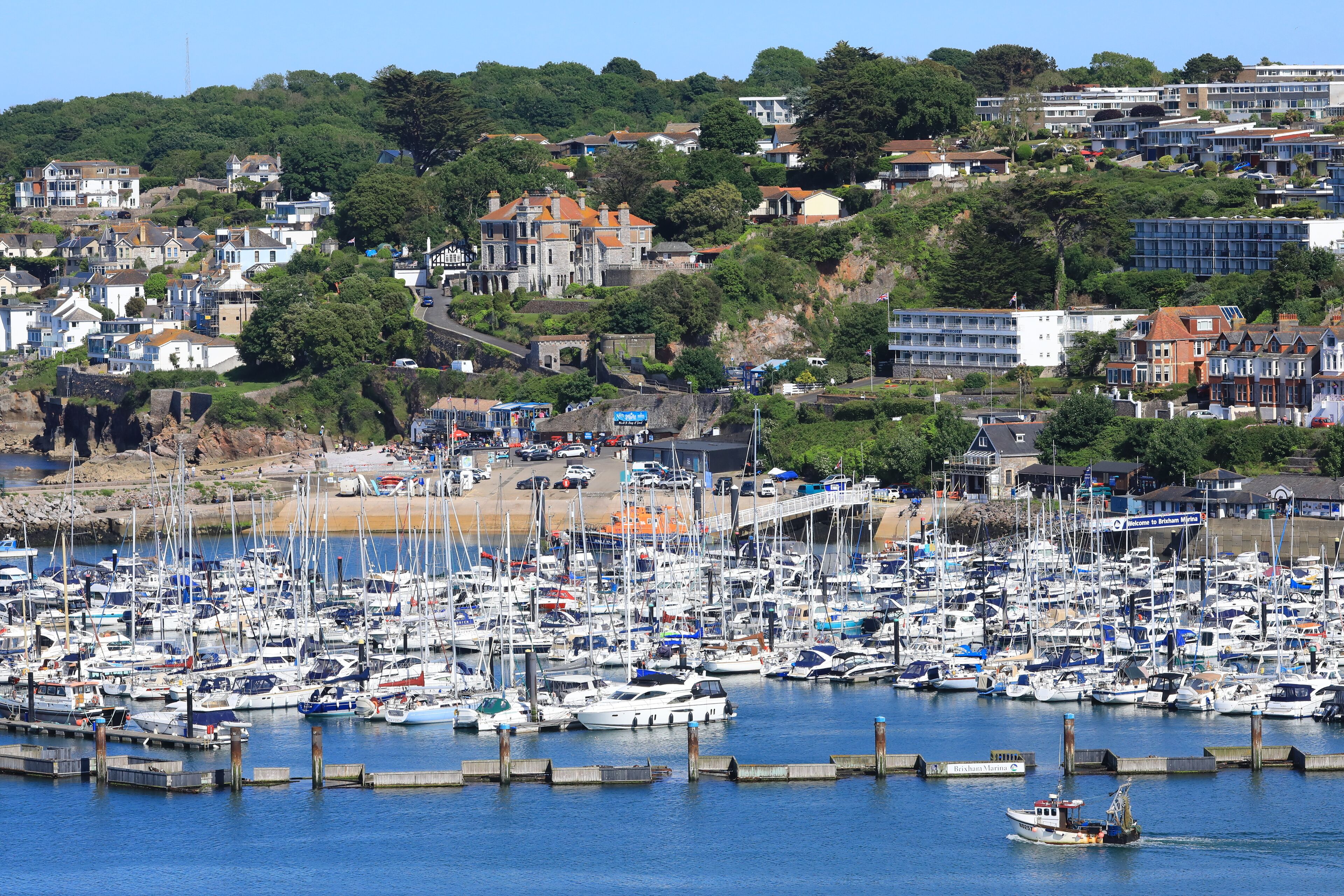 A marina with numerous boats docked, surrounded by residential buildings and greenery.