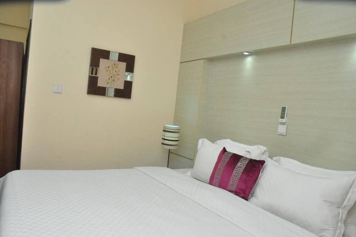 A hotel room with a bed, a wall-mounted artwork, a bedside lamp, and a light switch.