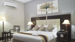 A hotel room with a large bed, two bedside tables with lamps, a chair, and a wall-mounted air conditioner. - Benny Hotel (Lagos)