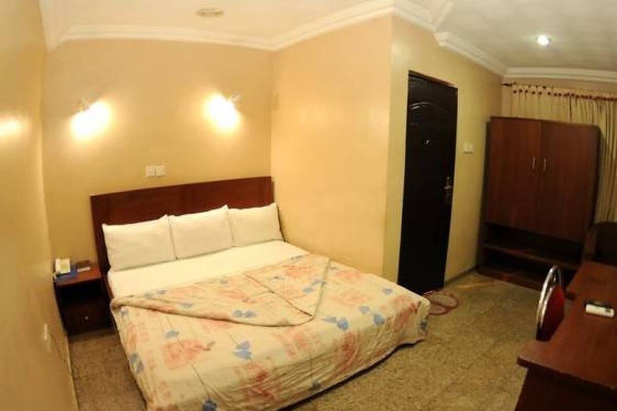 A hotel room with a bed, a nightstand, a wardrobe, and a desk.
