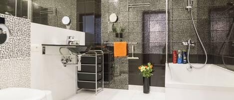 A modern bathroom with a large bathtub, a toilet, a sink with a mirror, and a shower area.