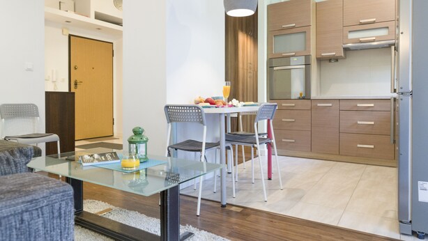 A modern kitchen with wooden cabinets, a dining table with chairs, and a refrigerator. - Apartament Praga Tower (Warsaw)
