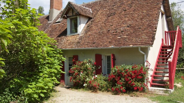 Une maison traditionnelle avec un toit à forte pente, une cheminée bien visible et un escalier rouge menant à l’entrée.