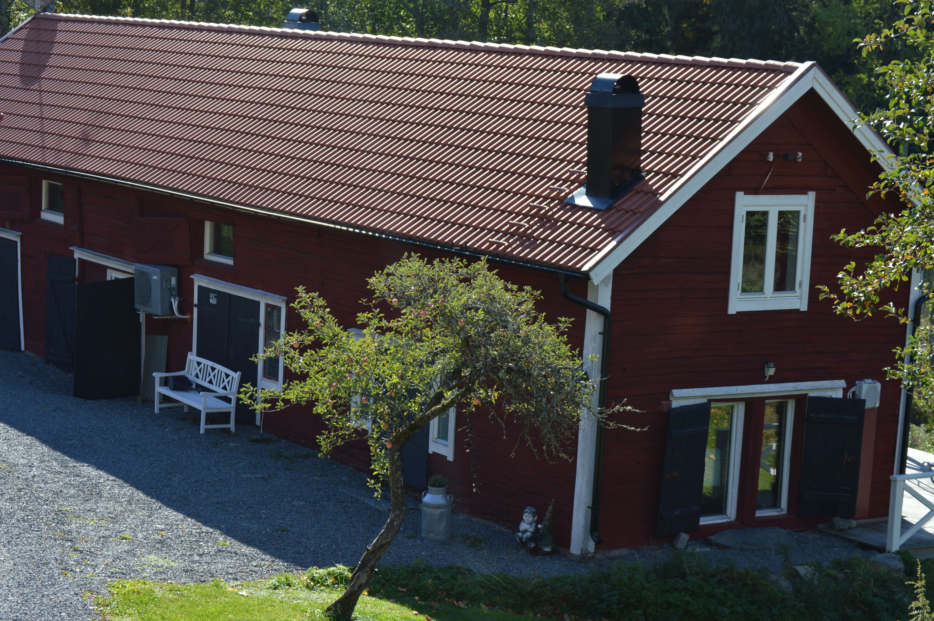 A red building with a sloped roof, a bench, and a tree in front.