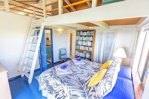 Un dormitorio con techo estilo loft, una estantería, una cama con colcha estampada y una escalera a la izquierda.