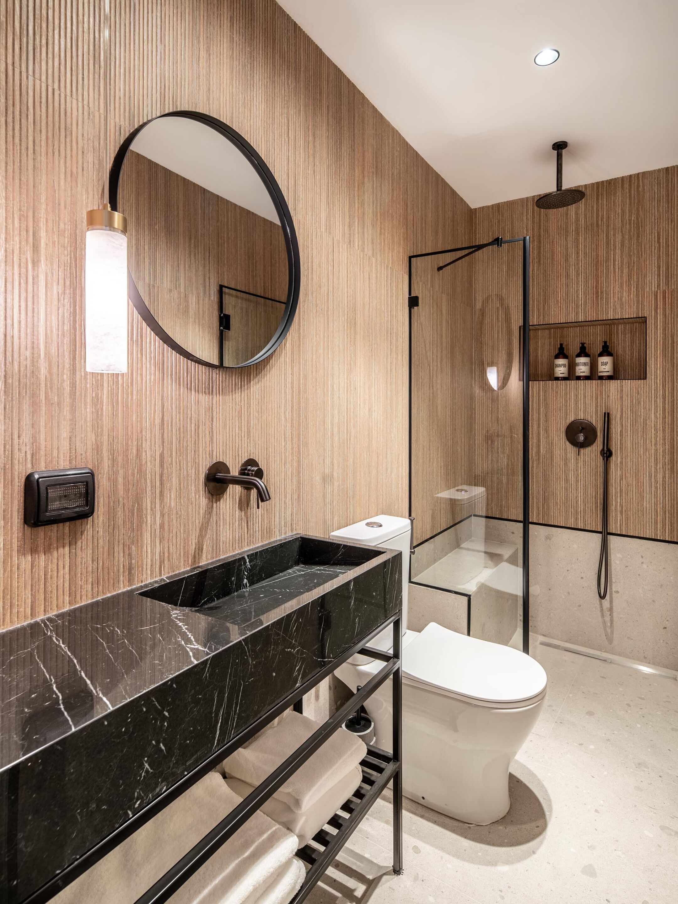 Et moderne badeværelse med en sort marmorvask, et rundt spejl, en glasafskærmet brusekabine og et toilet.