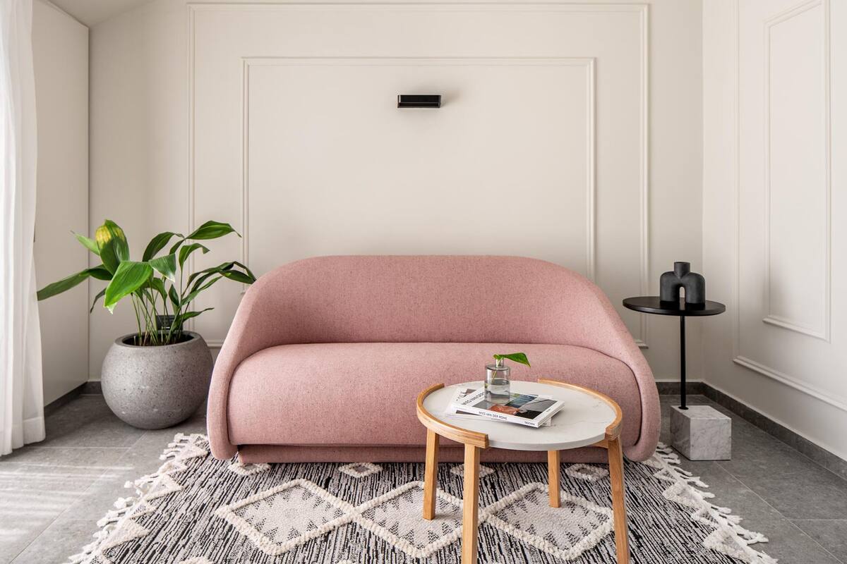 A modern living room with a pink sofa, a round wooden coffee table, a potted plant, and a small side table.