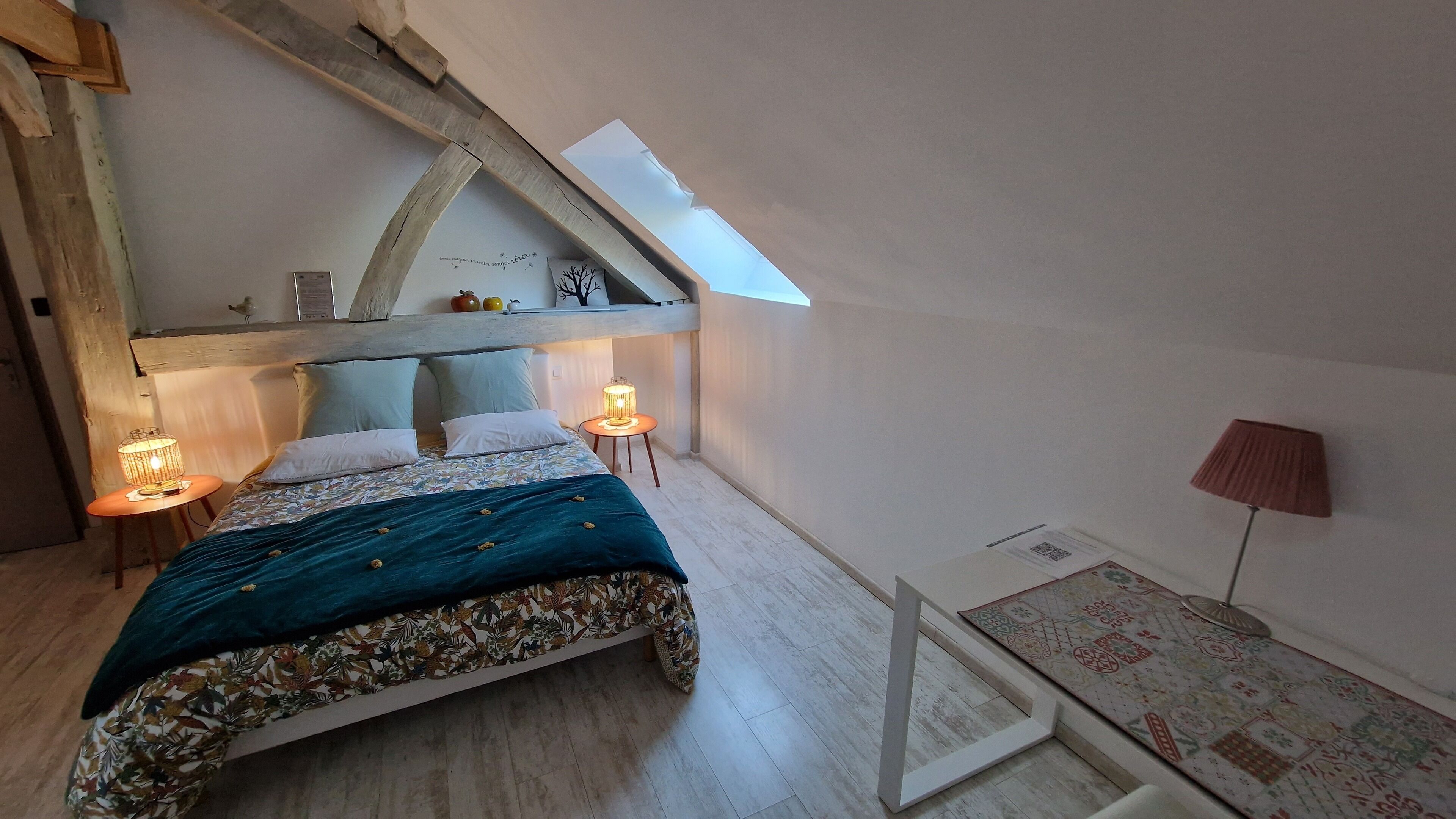 A bedroom with a sloped ceiling, a bed with a floral bedspread, two bedside lamps, and a small table with a lamp.