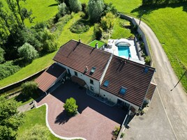 Vista aérea de uma casa com piscina, cercada por vegetação e uma entrada em curva.