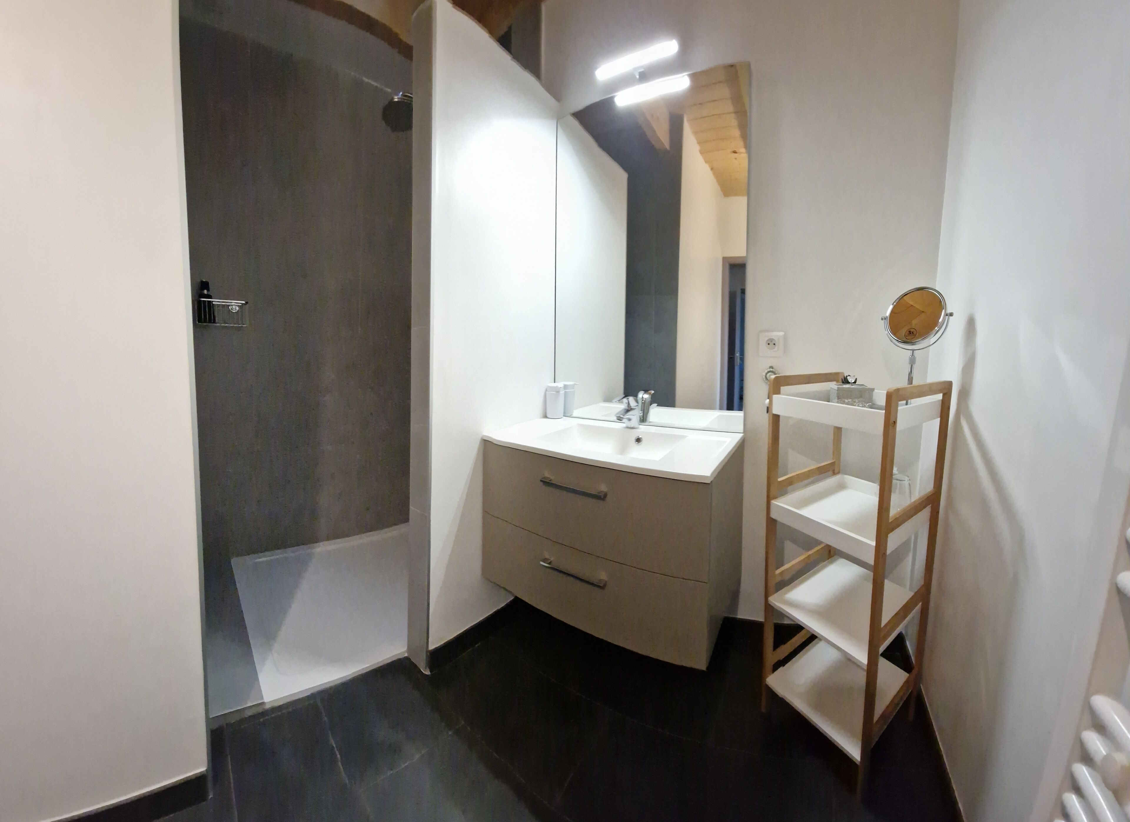 Une salle de bain moderne avec une douche, un meuble-lavabo avec un miroir et une étagère en bois.
