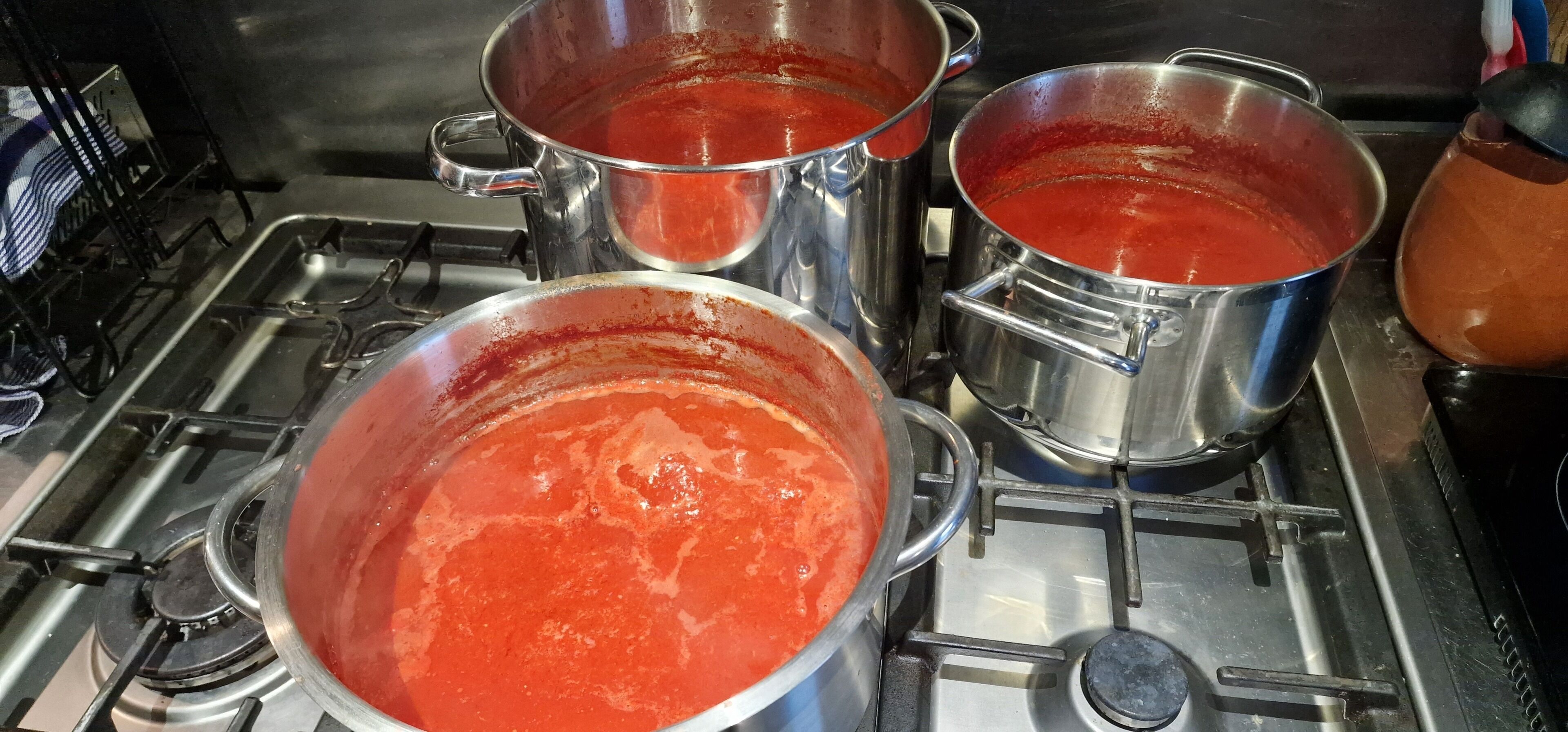 Una cocina con ollas de acero inoxidable sobre una estufa, una de ellas con salsa roja.