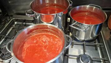Una cocina con ollas de acero inoxidable sobre una estufa, una de ellas con salsa roja.