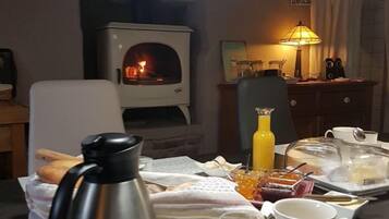 Une table accueillante, dressée pour le petit-déjeuner, avec un four à bois, une cafetière et une variété d’aliments pour le petit-déjeuner.