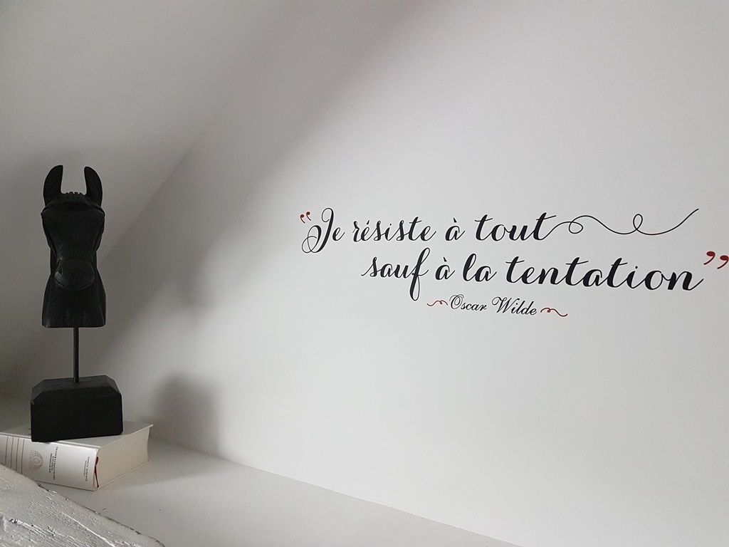 A wall with a quote in French, a black sculpture, and a white box with a book.