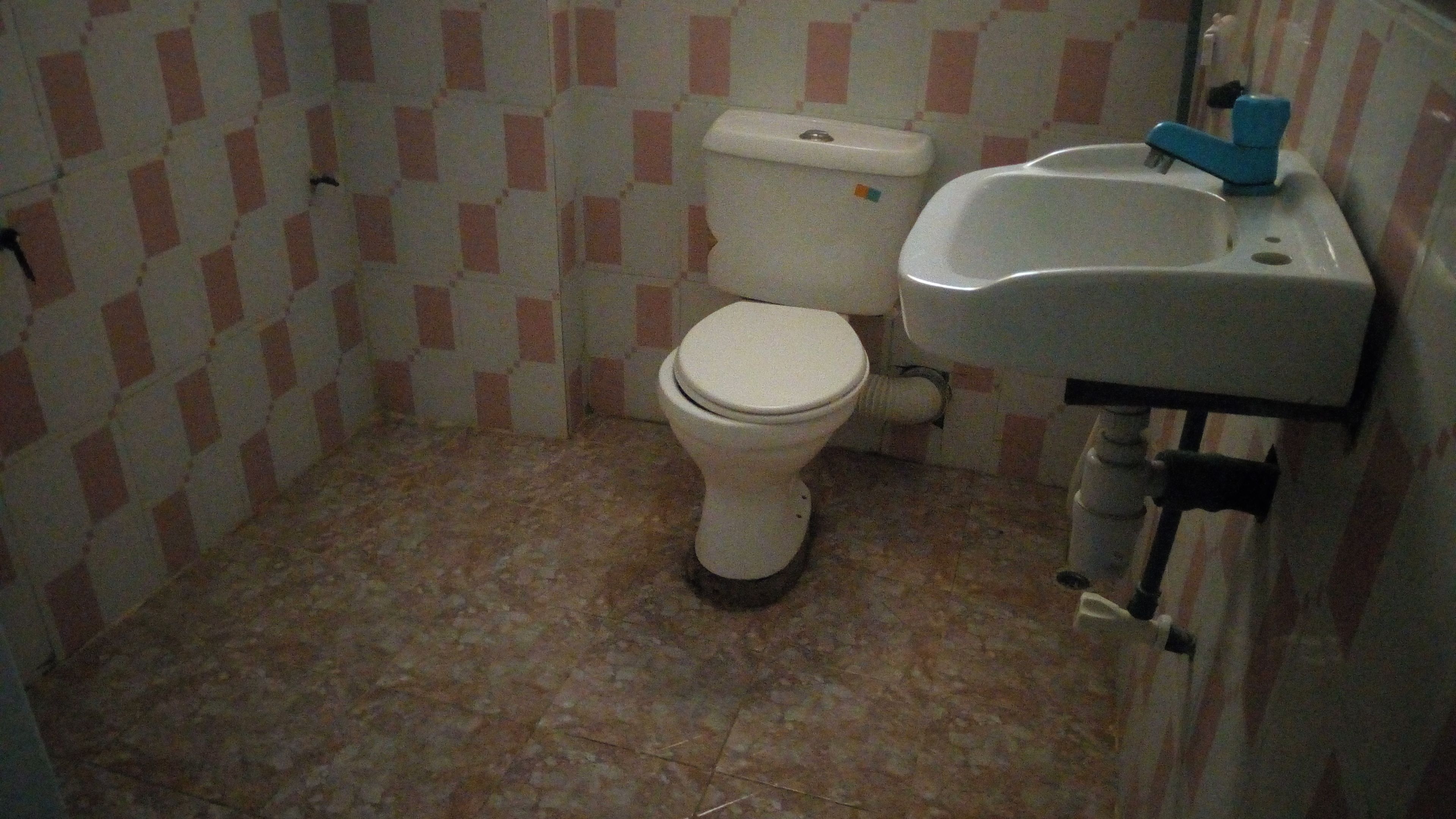 Egy kis fürdőszoba, amelyben WC, mosdókagyló és csempézett padló található.