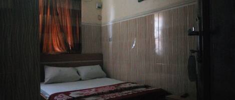 A small, dimly lit bedroom with a single bed, a wooden headboard, and a curtain partially drawn to the side.