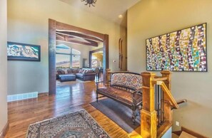 A spacious living area with a large window, a patterned rug, and a staircase with wooden railings. - Unobstructed Lake View 10 min to Snowbasin, Sleeps 12 (Huntsville)