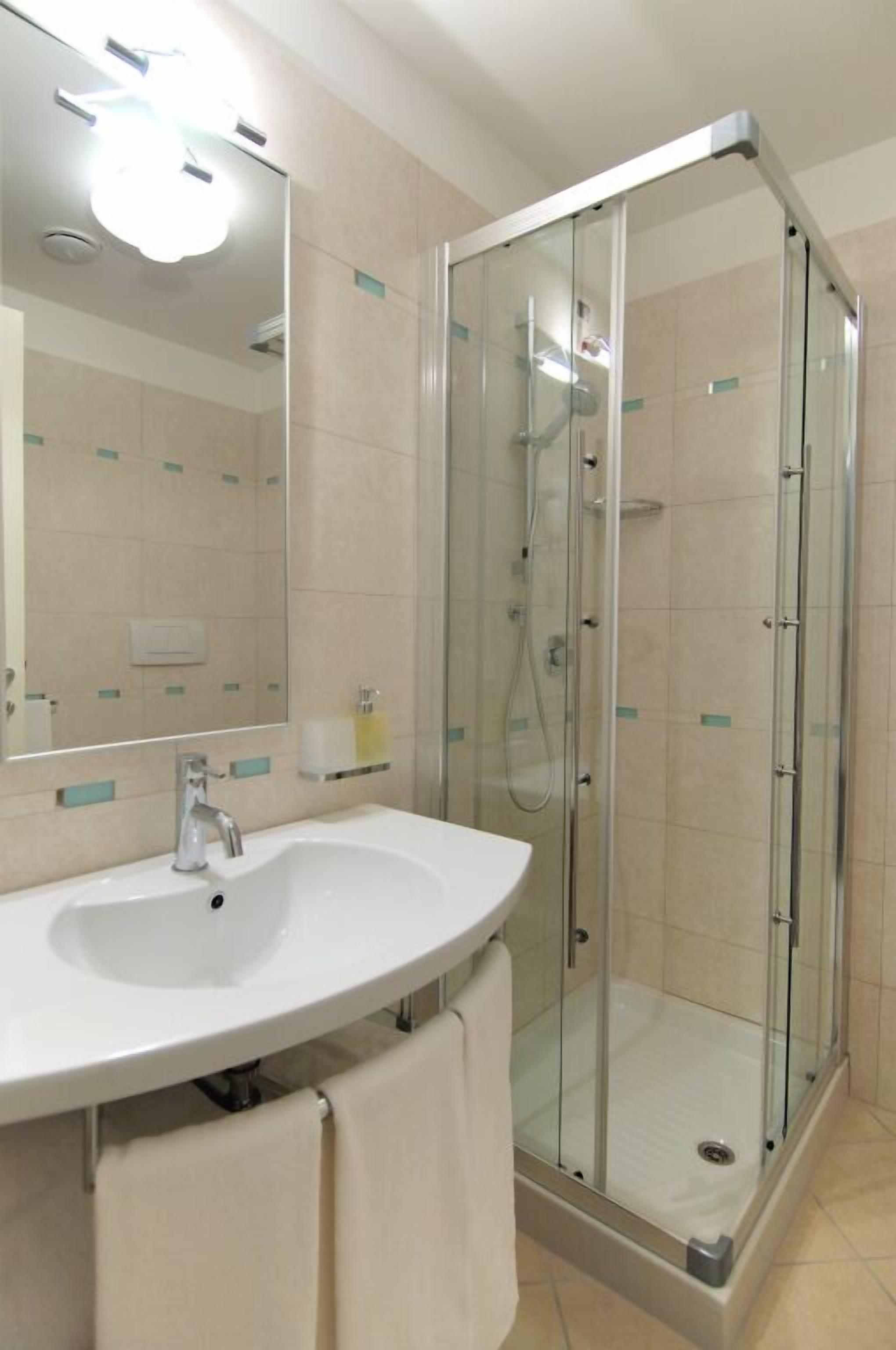 Un bagno moderno con doccia vetrata, un lavandino bianco e uno specchio sopra al lavandino.