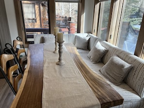 Una mesa de comedor de madera con velas, un sofá con cojines estampados y vistas al exterior a través de amplias ventanas.