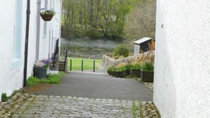 Un étroit sentier de pierres mène à un bâtiment blanc orné d’un panier à fleurs suspendu.