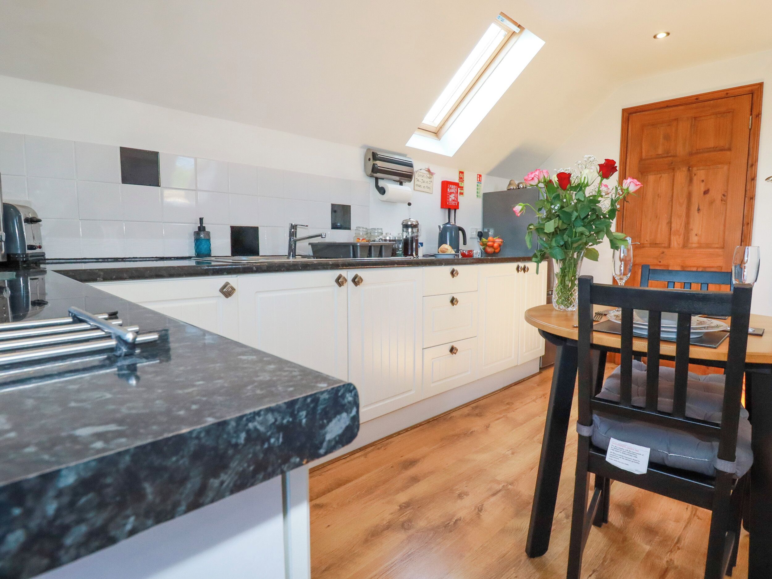 A modern kitchen with white cabinets, a black countertop, and a wooden dining table with chairs.