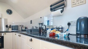 Een keuken met witte kastjes, een magnetron, een waterkoker en een klok aan de muur.