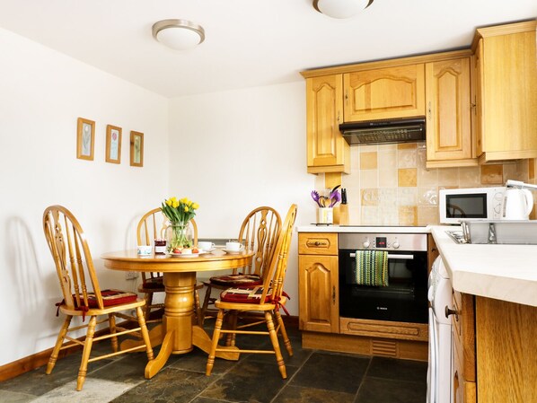 Een keuken met houten kasten, een Bosch oven, een magnetron en een eethoek met een ronde tafel en houten stoelen.
