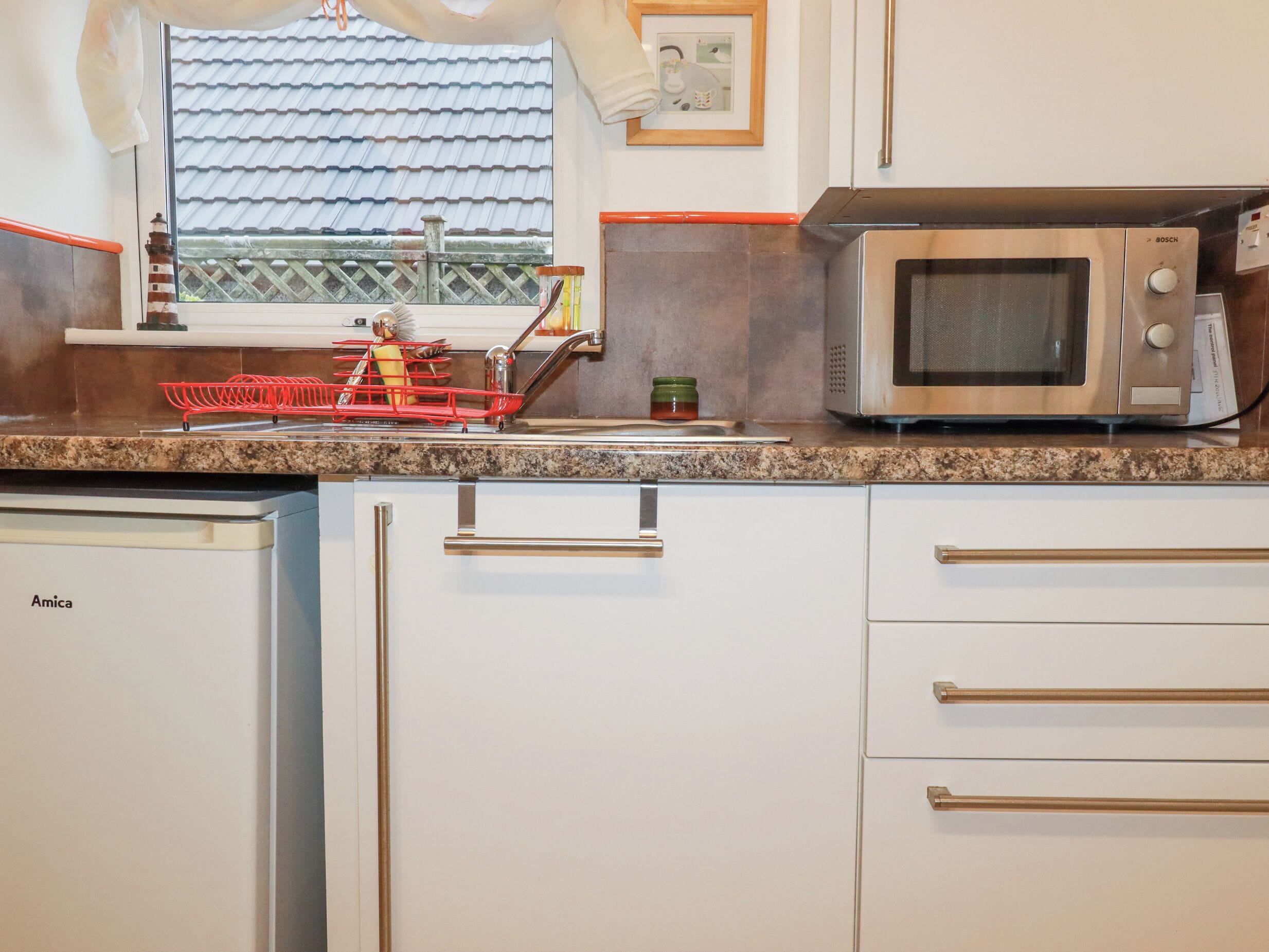 A kitchen with a Bosch microwave, a dish rack, and a sink.