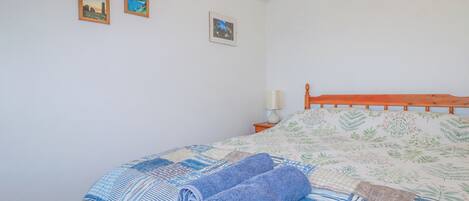 A bedroom with a wooden bed, a nightstand with a lamp, and two framed pictures on the wall.