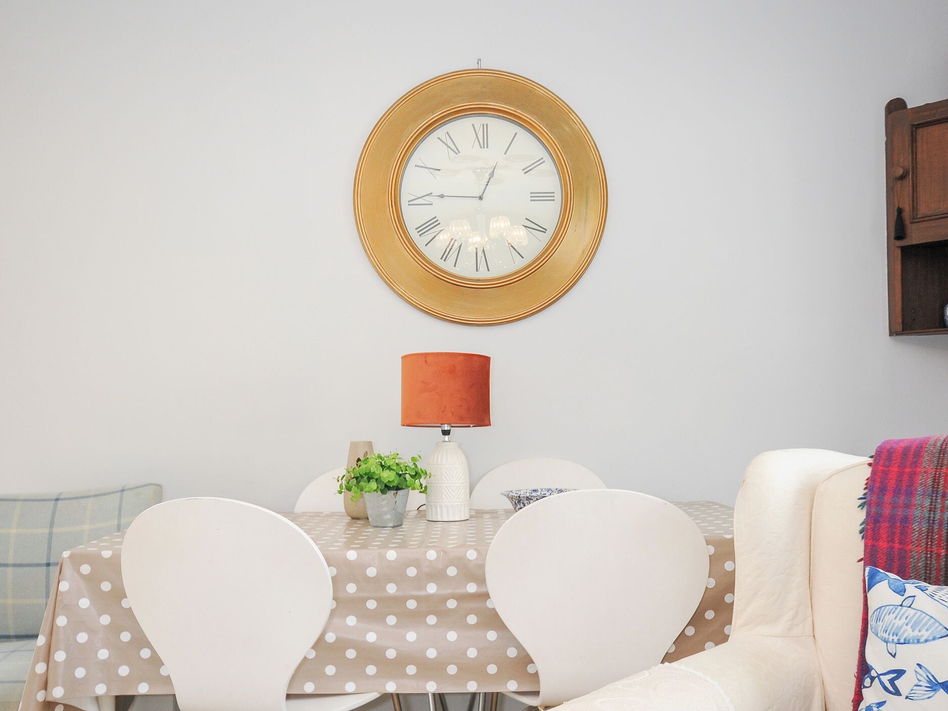 Un coin repas avec une table ronde, des chaises, une horloge, une lampe et une petite plante.