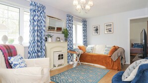 A cozy living room with a fireplace, a sofa, a blue patterned rug, and a television. - No. 1 The Heathers (Liskeard)
