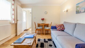 A living room with a grey sofa, a wooden coffee table, a dining table with two chairs, and a painting on the wall. - 19 Cormorant Drive (St Austell)