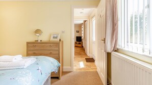 A bedroom with a bed, a dresser, a mirror, and a window with curtains. - 19 Cormorant Drive (St Austell)