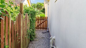 A narrow gravel path leading to a wooden gate, surrounded by a wooden fence and lush greenery. - 19 Cormorant Drive (St Austell)