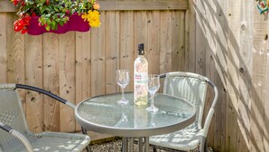 A round glass table with two wicker chairs, a bottle of Black Flower wine, and two wine glasses on the table. - 19 Cormorant Drive (St Austell)