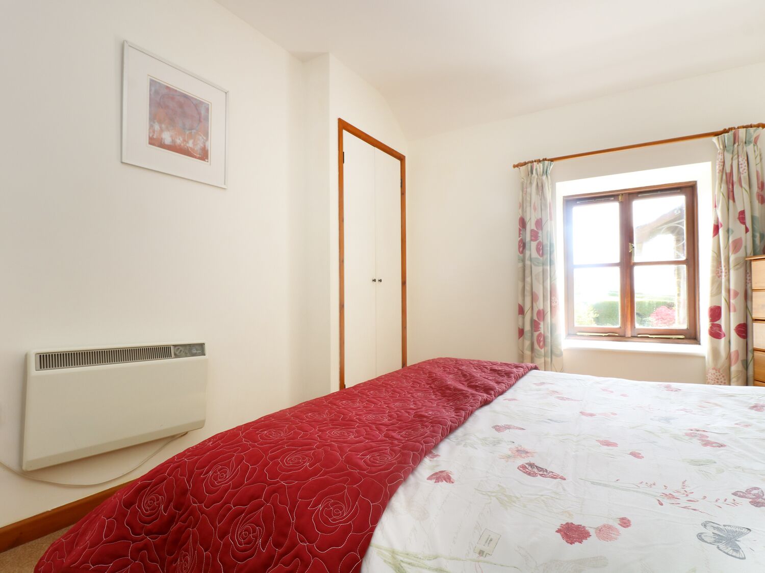 A bedroom with a bed, a radiator, a door, and a window with floral curtains.