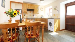 A kitchen with wooden cabinets, a washing machine, and a dining table with chairs. - The Old Granary (Launceston)