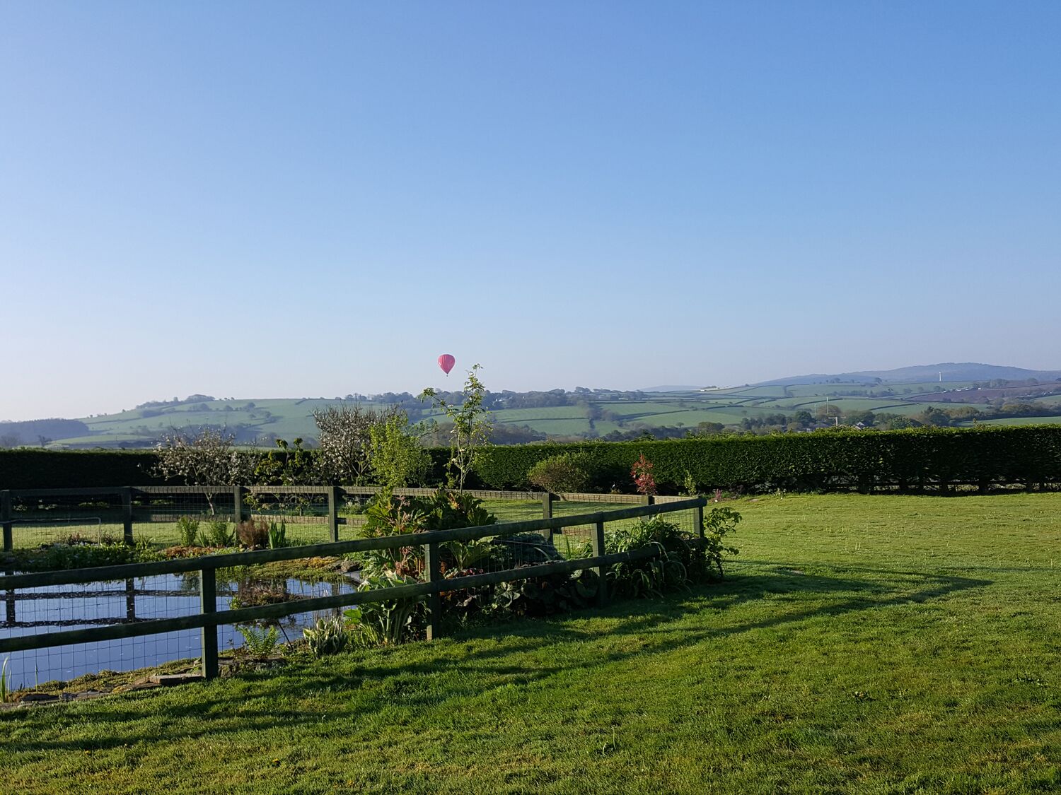A rural landscape with a clear sky, a pond, and a fence.
