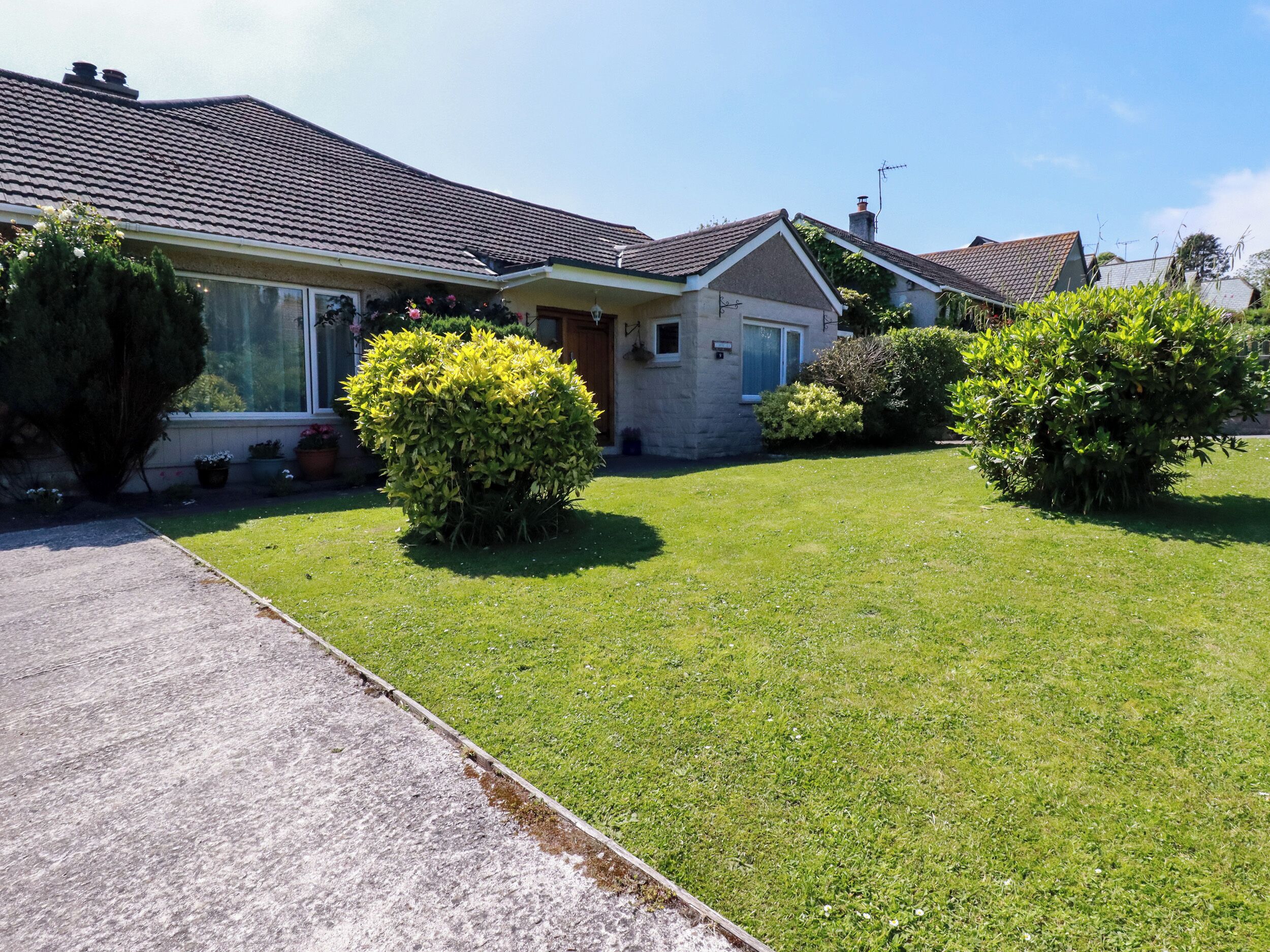 A residential house with a well-maintained lawn, a driveway, and a small garden area with bushes.