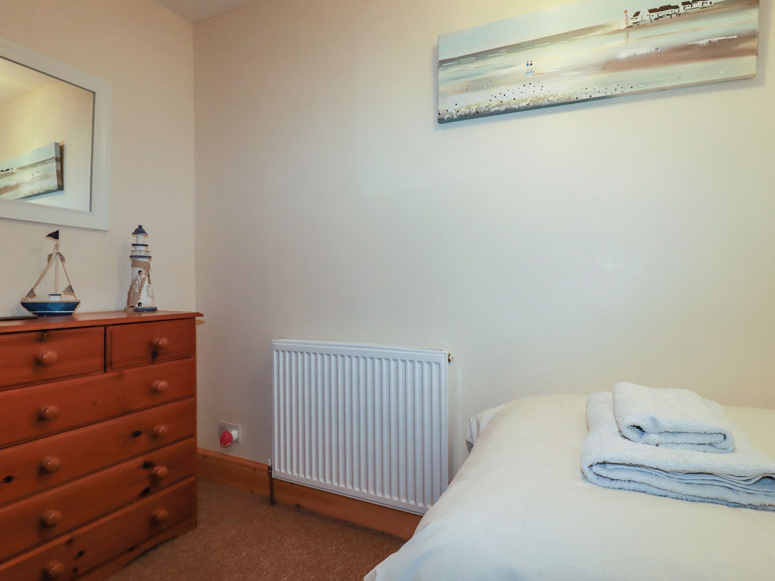 Une chambre à coucher avec un lit, une commode, un radiateur et un tableau accroché au mur.