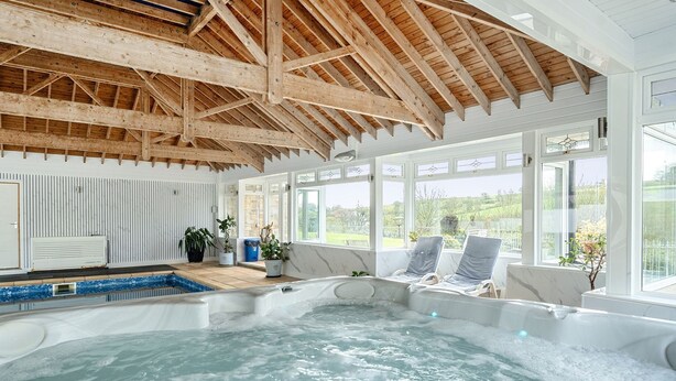 A spa area with a hot tub, wooden ceiling beams, and large windows.