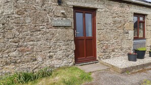 A stone building with a wooden door and window, a sign reading "BADGERS SETT", and potted plants outside.